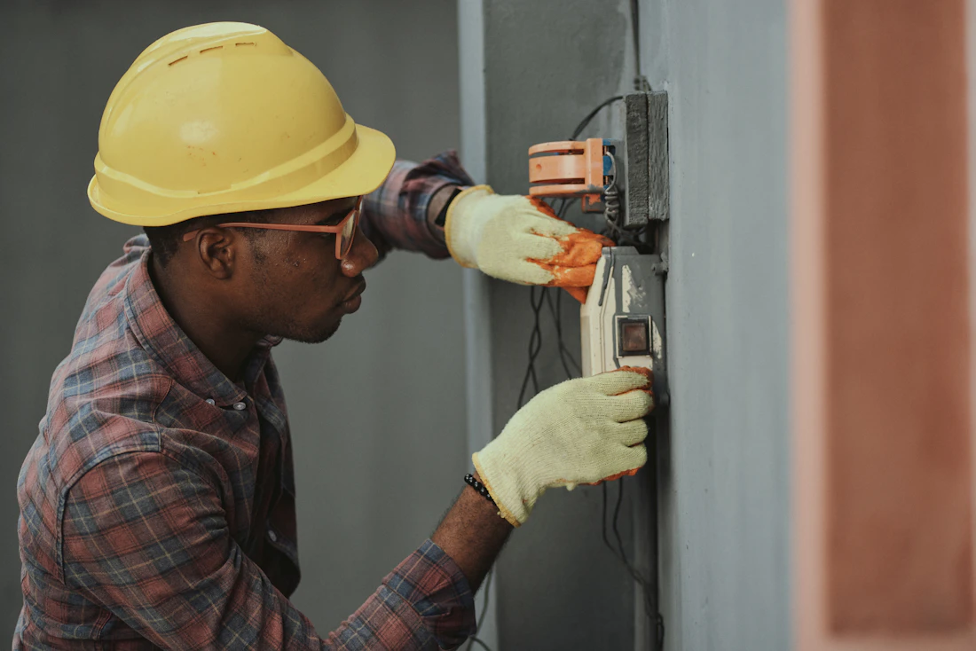 An electrician in a hard hat installing a fixture on a wall