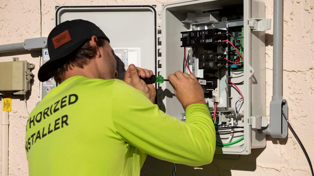 An electrician in a bright shirt working inside an electrical panel