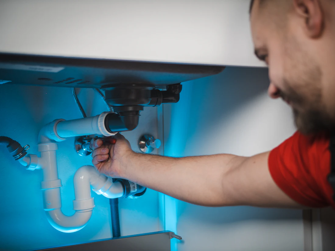 A plumber's hands fixing pipes under a sink