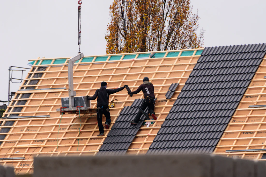 Workers installing dark roof tiles on a new roof frame