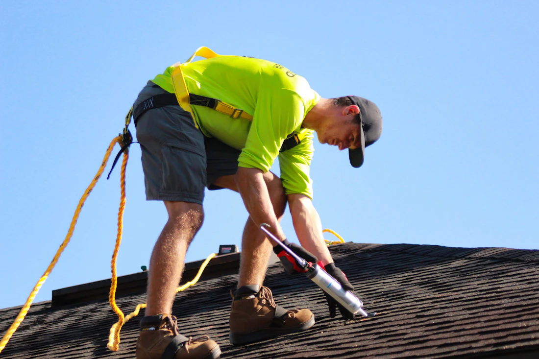 A roofer in a bright shirt working on a shingled roof